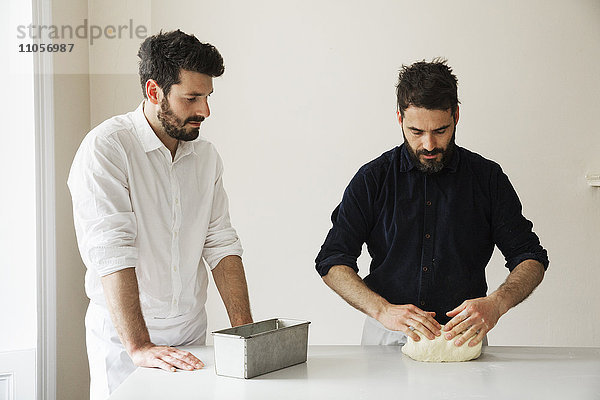 Zwei Bäcker  die an einem Tisch stehen und Brotteig kneten  eine Backform aus Metall.