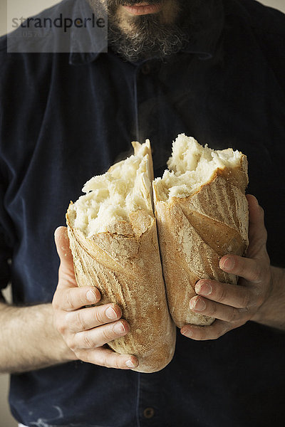 Nahaufnahme eines Bäckers mit zwei frisch gebackenen Brotlaiben.