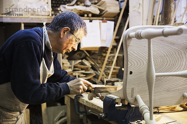 Mann  der an einer Werkbank in einer Schreinerei steht und an einem Holzstuhl arbeitet.