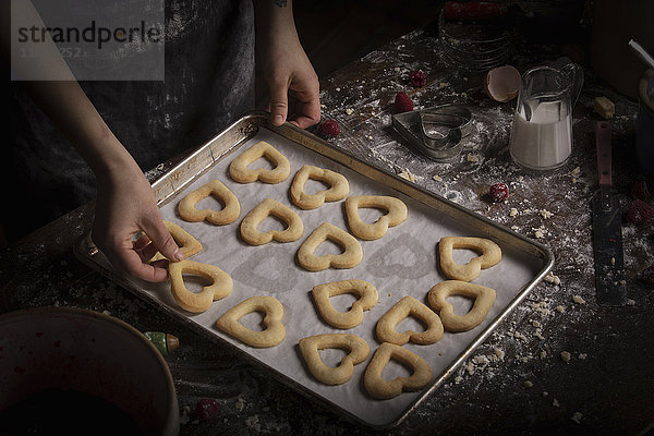 Valentinstag backen  Frau arrangiert herzförmige Kekse auf einem Backblech.