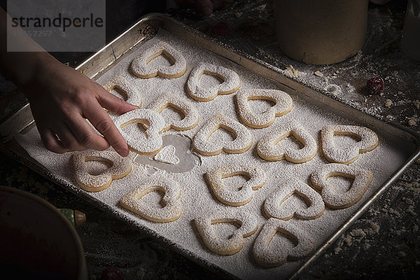 Valentinstag backen  Frau arrangiert herzförmige Kekse auf einem Backblech.