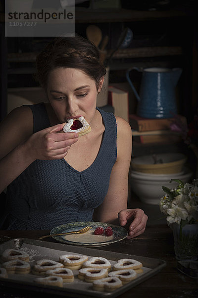 Valentinstag beim Backen  junge Frau sitzt in der Küche und isst einen herzförmigen Keks.