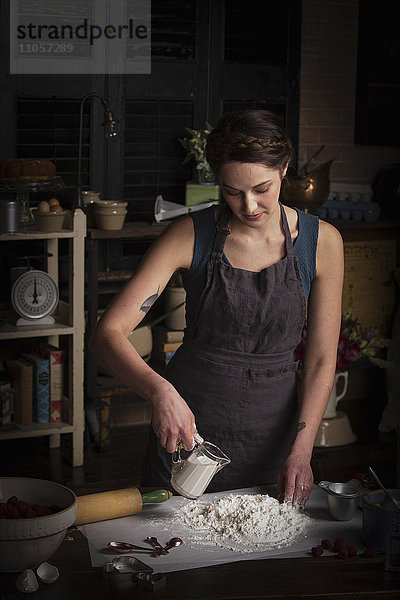Valentinstag beim Backen  junge Frau steht in einer Küche  bereitet Teig für Kekse zu  gießt Milch aus einer Kanne.
