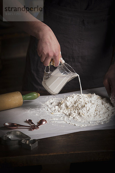 Valentinstag backen  Frau bereitet Teig für Kekse zu  gießt Milch aus einer Kanne.