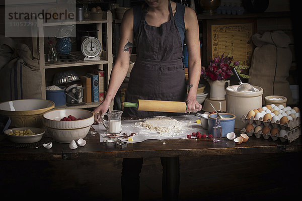 Valentinstag beim Backen  Frau steht in einer Küche und rollt mit einem Nudelholz Teig aus.