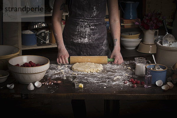 Valentinstag backen  Frau rollt mit einem Nudelholz Teig aus.