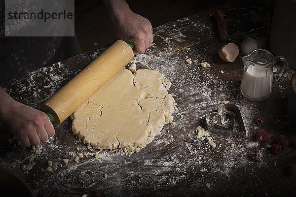 Valentinstag backen  Frau rollt mit einem Nudelholz Teig aus.