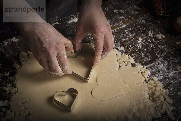 Valentinstag backen  Frau schneidet aus dem Teig herzförmige Kekse aus.