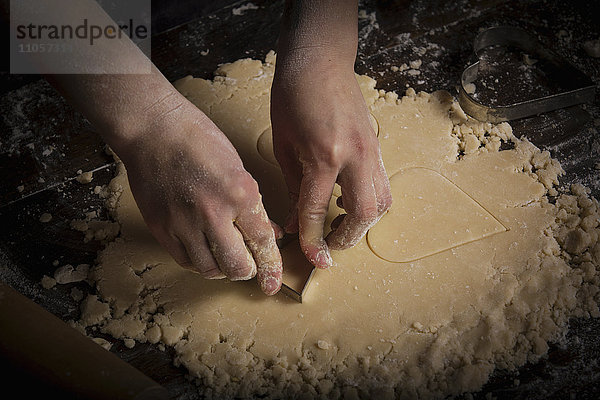 Valentinstag backen  Frau schneidet aus dem Teig herzförmige Kekse aus.