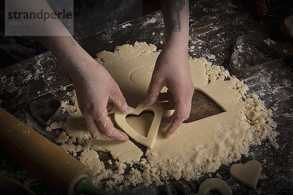 Valentinstag backen  Frau schneidet aus dem Teig herzförmige Kekse aus.