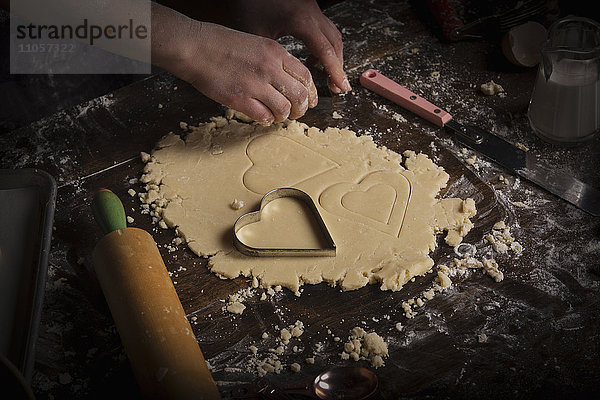 Backen zum Valentinstag. Frau schneidet auf einer bemehlten Fläche herzförmige Kekse aus Teig aus.