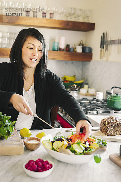 Eine Frau in einer Küche  die ein Salatgericht mit frischem Gemüse zubereitet.