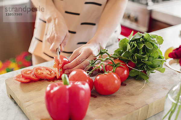 Eine Person an einer Küchentheke  die Salat zubereitet und frische Tomaten schneidet.