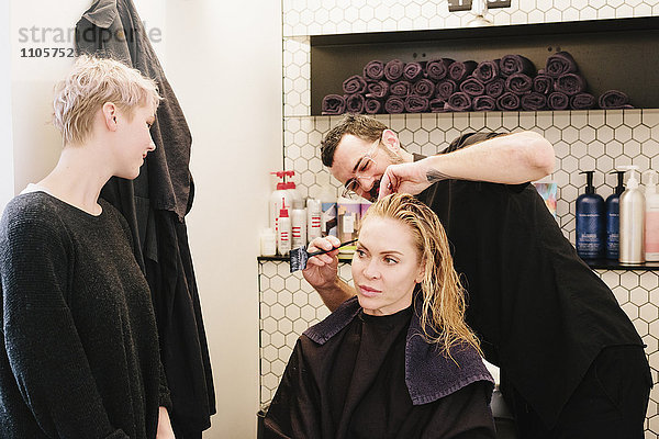 Ein Friseur  der in einem Friseursalon einer Frau die Haare schneidet.