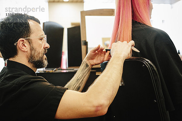 Eine Friseurin mit einer Kundin  schneidet ihr langes  glattes Haar  schneidet die Enden ab.