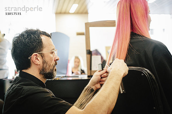 Eine Friseurin schneidet zusammen mit einer Kundin die Enden ihrer langen  rosa gefärbten  glatten Haare.