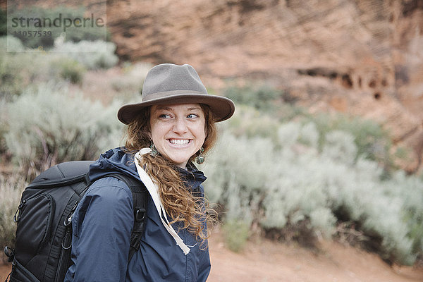 Lächelnde Frau mit rotbraunem Haar  die einen Hut trägt und einen Rucksack trägt  wandert in einem Canyon.
