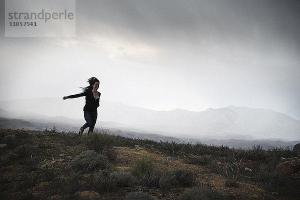 Frau rennt in einer Prärie unter bewölktem Himmel.