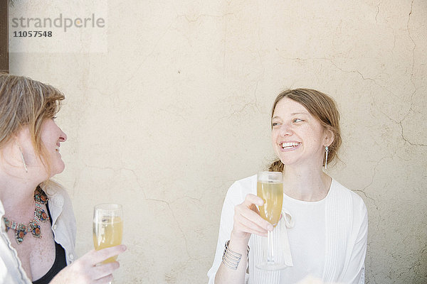 Zwei Frauen sitzen an einem Tisch  lächeln sich an und halten Gläser mit Champagner in der Hand.