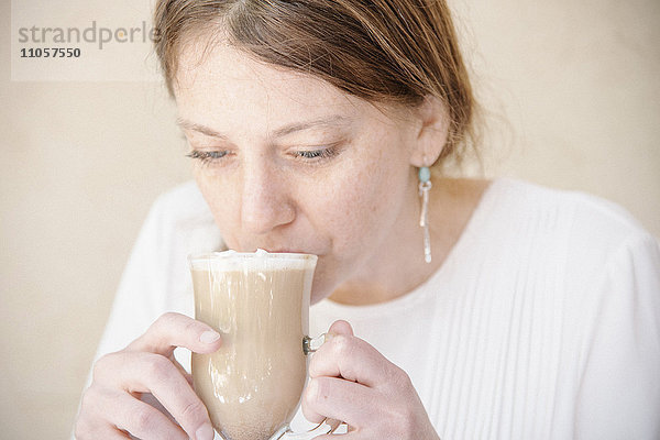 Porträt einer Frau mit rotbraunem Haar  die einen Café Latte trinkt.