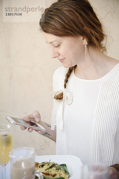 Porträt einer Frau mit langen  rotbraunen Haaren in einem Zopf  die auf ihr Handy schaut.