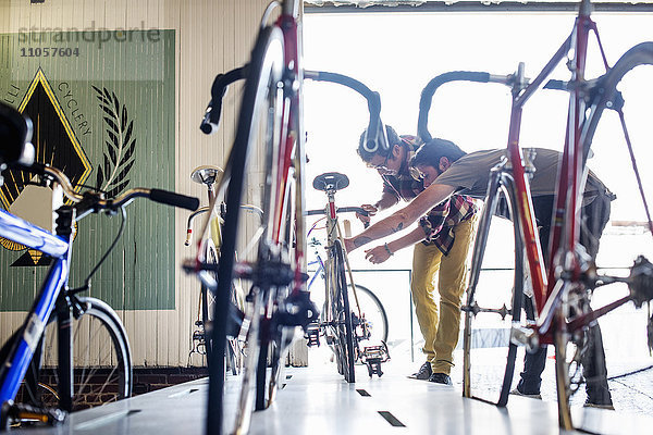Ein Mann  der in einer Fahrradwerkstatt arbeitet und zusammen mit einem Kunden ein Fahrrad überprüft.