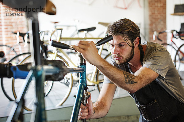 Ein Mann  der in einer Fahrradwerkstatt arbeitet und den Rahmen des Fahrrads überprüft.