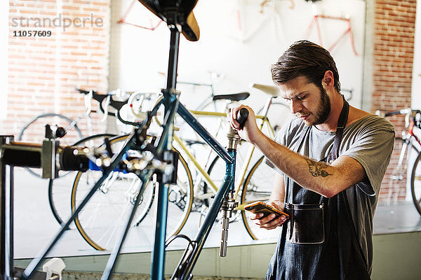 Ein Mann  der in einer Fahrradwerkstatt arbeitet und pausiert  um seine Nachrichten zu überprüfen.