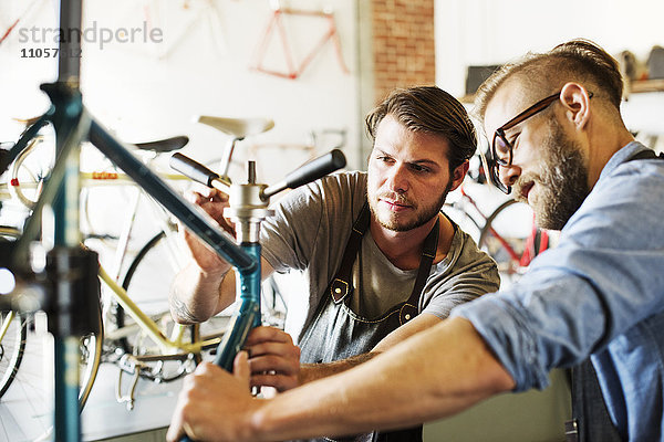 Zwei Männer in einer Fahrradwerkstatt  die sich ein Fahrrad anschauen.
