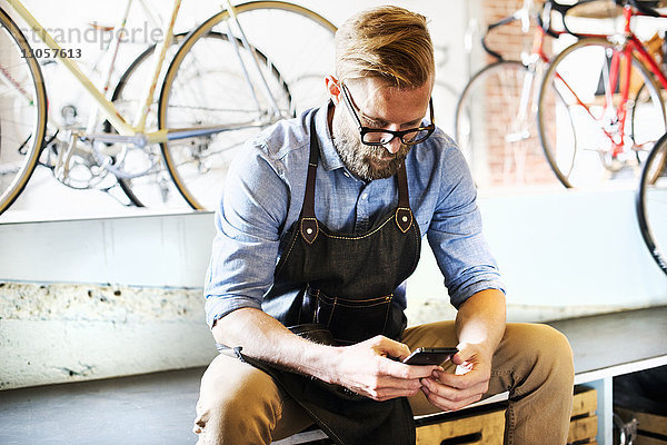 Ein Mann  der in einer Fahrradwerkstatt arbeitet und sein Telefon auf Nachrichten überprüft. Kaffeepause.