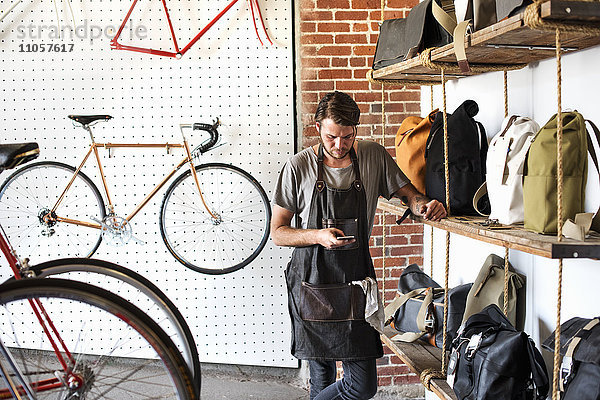 Ein Mann  der in einer Fahrradwerkstatt arbeitet und auf sein Smartphone schaut.