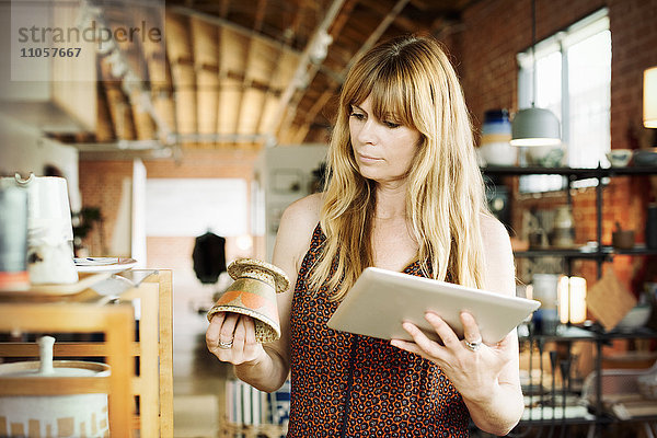 Frau in einem Geschäft  die ein digitales Tablett und einen kleinen Keramiktopf in der Hand hält.