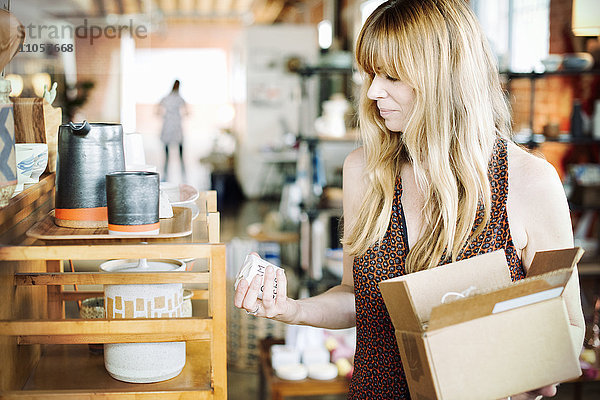 Frau in einem Geschäft  die einen kleinen Karton mit Waren in der Hand hält.