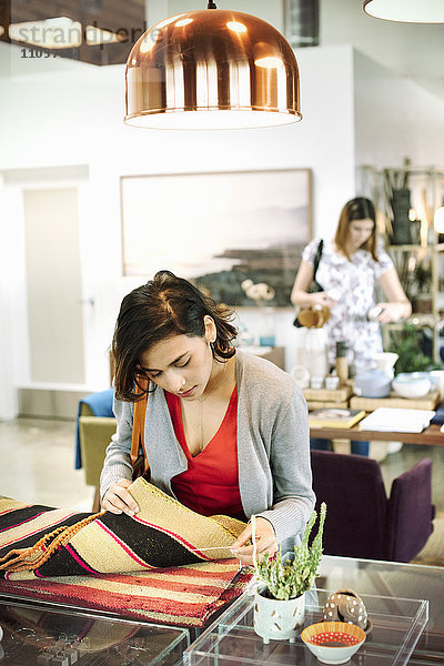 Junge Frau in einem Geschäft  die sich kleine gestreifte Teppiche ansieht.