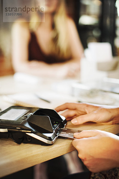 Nahaufnahme einer Frau  die in einem Geschäft ein Kreditkartenlesegerät benutzt.