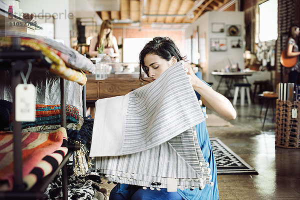 Junge Frau in einem Geschäft  die eine gestreifte Tischdecke in der Hand hält.