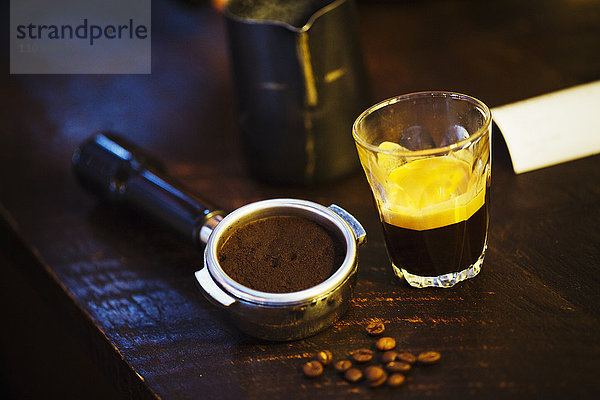 Spezialisiertes Kaffeehaus. Ein Kaffeemaschinen-Satzhalter  ein Haufen Kaffeebohnen und eine Glastasse mit Espresso-Kaffee.