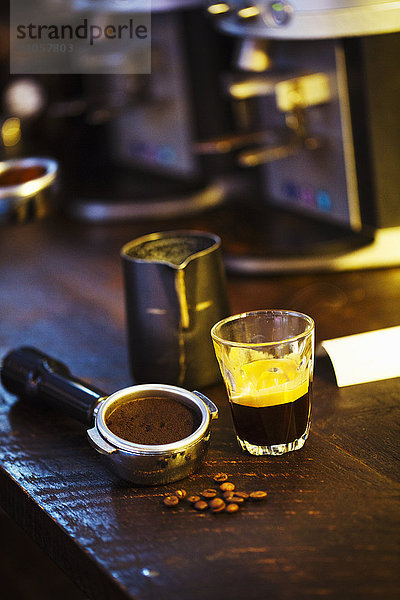 Spezialisiertes Kaffeehaus. Ein Kaffeemaschinen-Satzhalter  ein Haufen Kaffeebohnen und eine Glastasse mit Espresso-Kaffee.