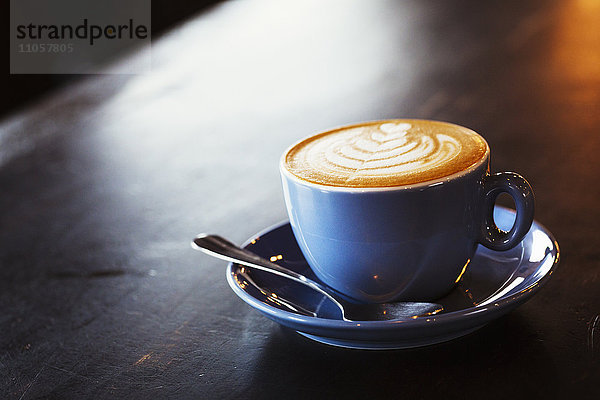 Spezialisiertes Kaffeehaus. Blaue Porzellantasse und Untertasse voller Kaffee  mit einem Blattmuster im Schaum.
