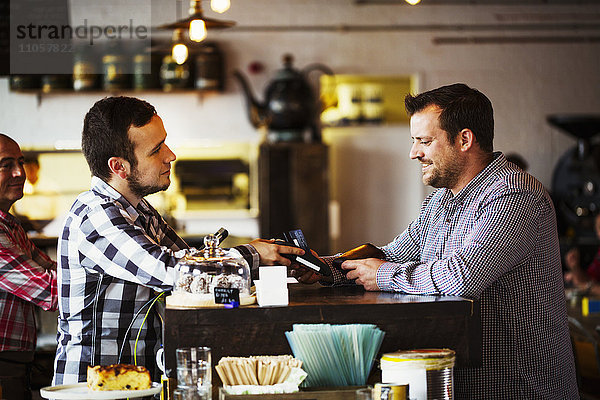Spezialisiertes Kaffeehaus. Zwei Männer  ein Barista und ein Klient unterhalten sich über dem Tresen des Cafés.