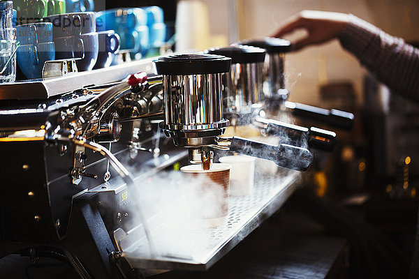 Spezialisiertes Kaffeehaus. Eine Person  die an einer großen Kaffeemaschine arbeitet  mit drei Perkolationsbehältern  Griffen und einem Rohr  das Dampf abgibt.