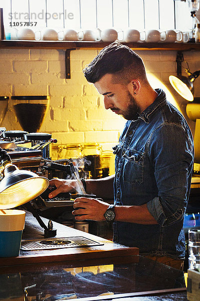 Spezialisiertes Kaffeehaus. Ein Mann  der Cappuccino zubereitet und die Milch mit einem Dampfgarer aufschäumt.