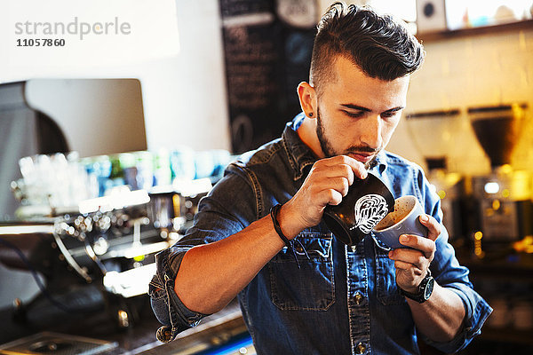 Spezialisiertes Kaffeehaus. Ein Mann  der Cappuccino zubereitet und Schaummuster in einer Kaffeetasse erzeugt.