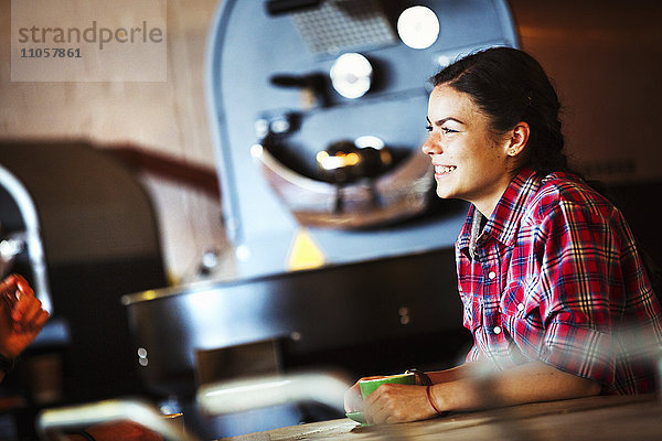 Spezialisiertes Kaffeehaus. Eine Frau sitzt an einem Tresen bei einer Röstmaschine.