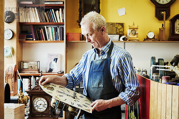 Ein Uhrmacher  der seine Arbeit in der Werkstatt betrachtet.