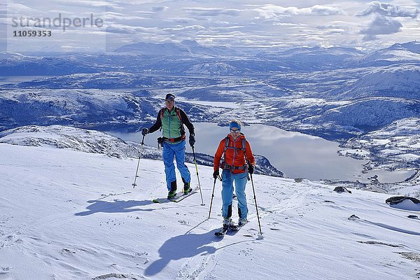 Zwei Skitourengeher im Aufstieg zum Skarelvfjellet  Verschneite Berglandschaft mit Seen  Senja  Norwegen  Europa