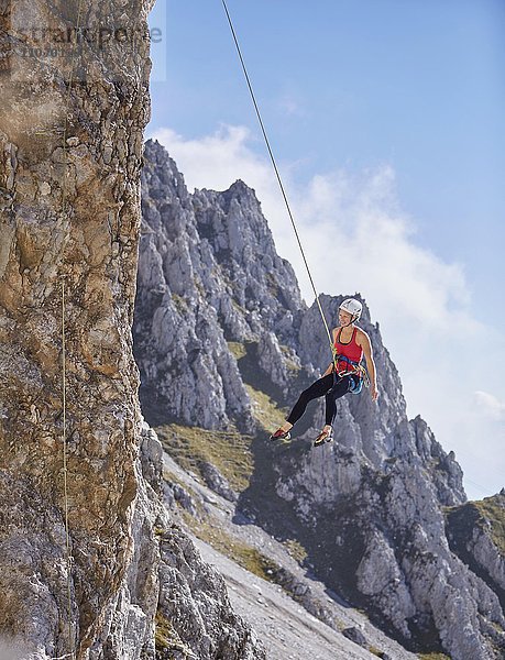 Kletterin mit Helm schwingt im Kletterseil an Felswand  Nordalpen  bei Innsbruck  Tirol  Österreich  Europa