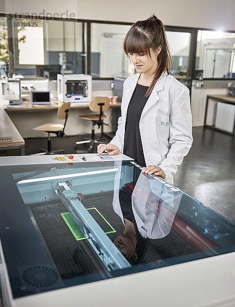 Technikerin  Frau 20-25 Jahre  mit weißem Laborkittel bedient einen Laser Cutter in einem Elektronik Labor  Wattens  Innsbrucker Land  Tirol  Österreich  Europa