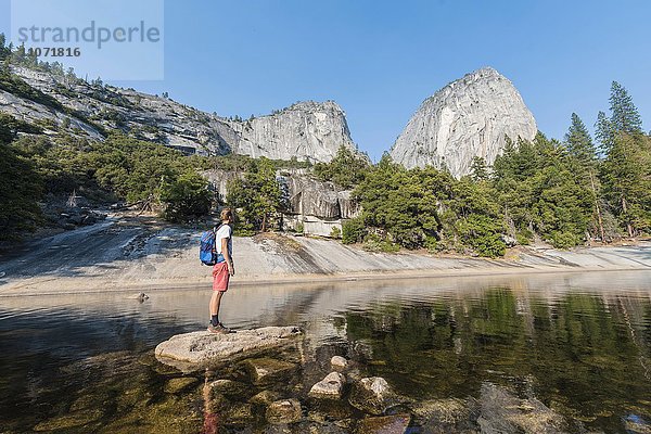 Junger Mann steht auf einem Stein mitten im Fluss Merced River  Liberty Cap  Mist Trail  Yosemite-Nationalpark  Kalifornien  USA  Nordamerika
