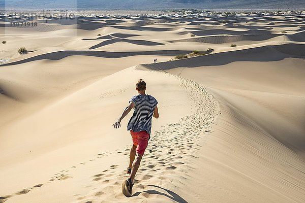 Junger Mann  Tourist läuft eine Sanddüne hinunter  Mesquite Flat Sand Dunes  Sanddünen  Death Valley  Death-Valley-Nationalpark  Kalifornien  USA  Nordamerika